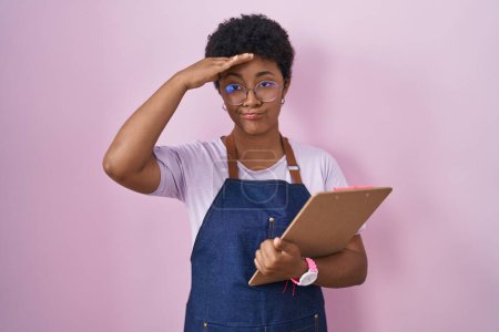 Photo for Young african american woman wearing professional waitress apron holding clipboard worried and stressed about a problem with hand on forehead, nervous and anxious for crisis - Royalty Free Image