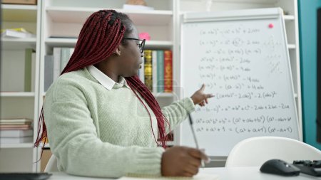 Téléchargez les photos : Femme africaine avec professeur de cheveux tressés donnant des leçons de mathématiques à la bibliothèque universitaire - en image libre de droit