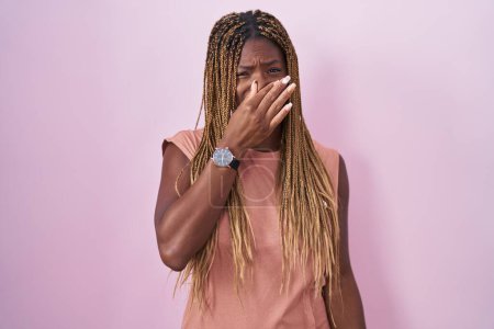 Photo for African american woman with braided hair standing over pink background smelling something stinky and disgusting, intolerable smell, holding breath with fingers on nose. bad smell - Royalty Free Image