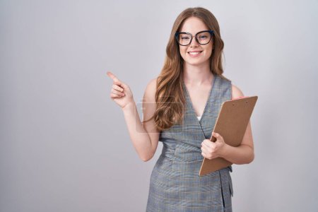 Photo for Caucasian woman wearing glasses and business clothes cheerful with a smile on face pointing with hand and finger up to the side with happy and natural expression - Royalty Free Image