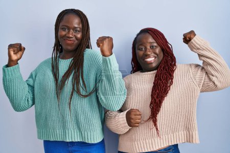 Photo for Two african woman standing over blue background showing arms muscles smiling proud. fitness concept. - Royalty Free Image