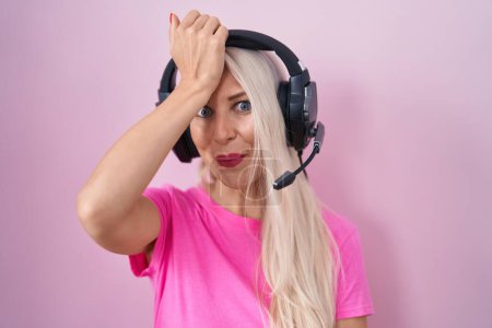 Téléchargez les photos : Femme caucasienne écoutant de la musique à l'aide d'écouteurs surpris avec la main sur la tête pour erreur, rappelez-vous erreur. oublié, mauvais concept de mémoire. - en image libre de droit