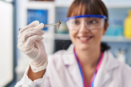 Photo for Young beautiful hispanic woman scientist smiling confident holding plant with tweezers at pharmacy - Royalty Free Image