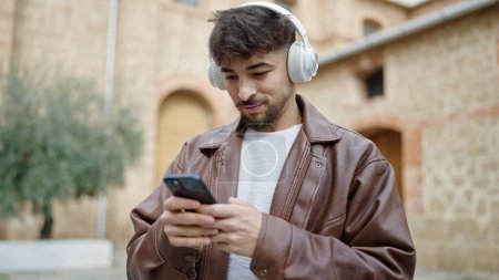 Téléchargez les photos : Jeune homme arabe écoutant de la musique avec une expression détendue dans la rue - en image libre de droit