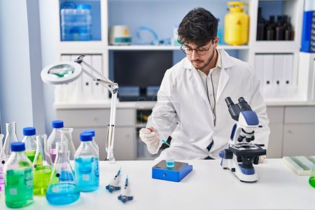 Téléchargez les photos : Jeune homme hispanique scientifique mesurant le liquide en laboratoire - en image libre de droit