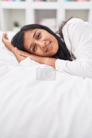 Foto de Joven hermosa mujer hispana sonriendo confiada acostada en la cama en el dormitorio - Imagen libre de derechos