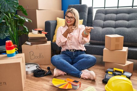 Photo for Young hispanic woman moving to a new home sitting on the floor pointing fingers to camera with happy and funny face. good energy and vibes. - Royalty Free Image
