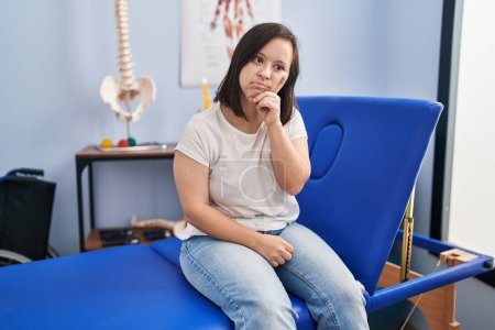 Photo for Hispanic girl with down syndrome at physiotherapy clinic serious face thinking about question with hand on chin, thoughtful about confusing idea - Royalty Free Image
