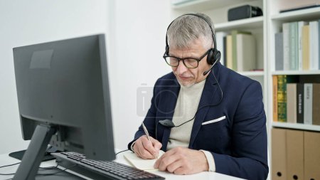 Photo for Middle age grey-haired man teacher having video call writing on notebook at university classroom - Royalty Free Image