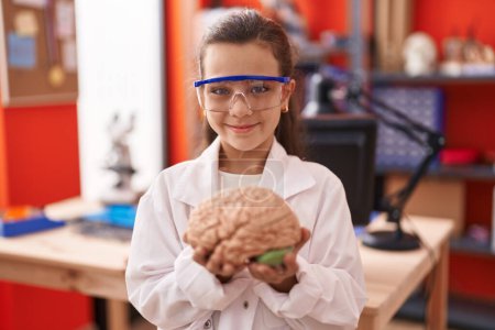 Photo for Little hispanic girl holding brain at science class at school smiling with a happy and cool smile on face. showing teeth. - Royalty Free Image