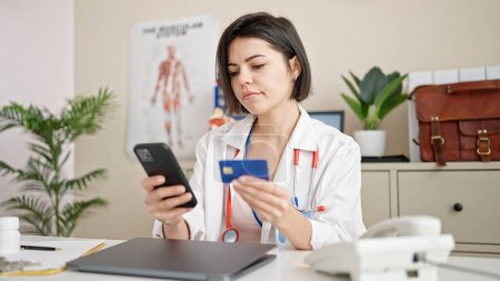 Téléchargez les photos : Jeune femme caucasienne médecin faisant des achats en ligne avec smartphone à la clinique - en image libre de droit