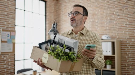 Foto de Hombre de mediana edad trabajador de negocios despedido celebración de la caja de cartón utilizando el teléfono inteligente en la oficina - Imagen libre de derechos