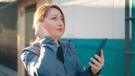 Photo for Young redhead woman wearing sportswear listening to music using smartphone at street - Royalty Free Image