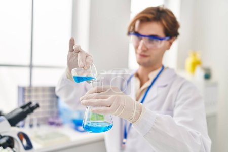 Téléchargez les photos : Young caucasian man scientist pouring liquid on test tube at laboratory - en image libre de droit