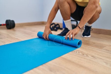 Photo for Young arab man rolling up yoga mat at sport center - Royalty Free Image