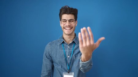 Téléchargez les photos : Jeune homme hispanique souriant confiant faire venir geste avec les mains sur fond bleu isolé - en image libre de droit