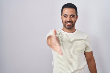 Foto de Hispanic man with beard standing over isolated background smiling friendly offering handshake as greeting and welcoming. successful business. - Imagen libre de derechos