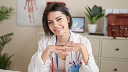 Foto de Mujer joven caucásica médico sentado en el escritorio sonriendo en la clínica - Imagen libre de derechos