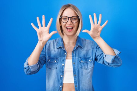 Téléchargez les photos : Jeune femme caucasienne debout sur fond bleu montrant et pointant vers le haut avec les doigts numéro dix tout en souriant confiant et heureux. - en image libre de droit