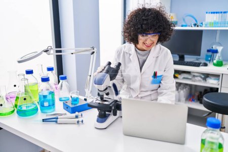 Photo for Young middle east woman scientist using laptop and microscope at laboratory - Royalty Free Image