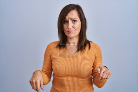 Photo for Middle age brunette woman standing wearing orange sweater pointing down looking sad and upset, indicating direction with fingers, unhappy and depressed. - Royalty Free Image