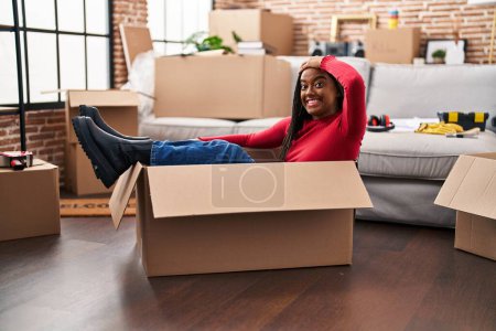 Photo for Young african american with braids moving to a new home inside of a cardboard box stressed and frustrated with hand on head, surprised and angry face - Royalty Free Image