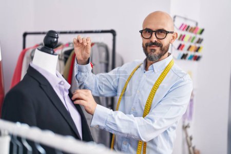 Téléchargez les photos : Jeune tailleur chauve souriant confiant travaillant à la boutique de tailleur - en image libre de droit