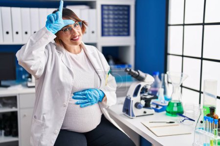 Foto de Mujer embarazada que trabaja en el laboratorio científico burlándose de las personas con los dedos en la frente haciendo gesto perdedor burlándose e insultando. - Imagen libre de derechos
