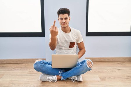 Foto de Young hispanic man using laptop at home showing middle finger, impolite and rude fuck off expression - Imagen libre de derechos