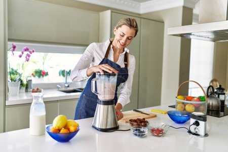 Photo for Young blonde woman smiling confident liquefying smoothie using bender at kitchen - Royalty Free Image