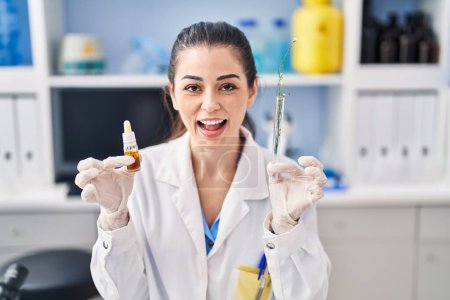 Foto de Mujer joven haciendo extracción de aceite de hierba en el laboratorio sonriendo y riendo en voz alta porque broma loca divertida. - Imagen libre de derechos