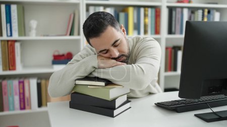 Téléchargez les photos : Young hispanic man student sleeping with head on books at library university - en image libre de droit