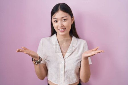 Téléchargez les photos : Chinoise jeune femme debout sur fond rose souriant joyeuse offrant les mains donnant assistance et acceptation. - en image libre de droit