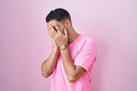 Téléchargez les photos : Jeune homme hispanique debout sur fond rose avec une expression triste couvrant le visage avec les mains tout en pleurant. concept de dépression. - en image libre de droit