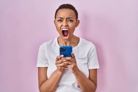 Téléchargez les photos : Belle femme afro-américaine utilisant smartphone en colère et fou hurlant frustré et furieux, criant de colère. rage et concept agressif. - en image libre de droit