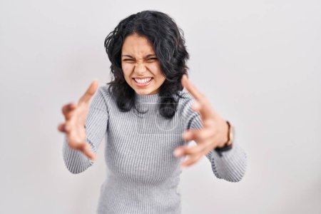 Photo for Hispanic woman with dark hair standing over isolated background shouting frustrated with rage, hands trying to strangle, yelling mad - Royalty Free Image