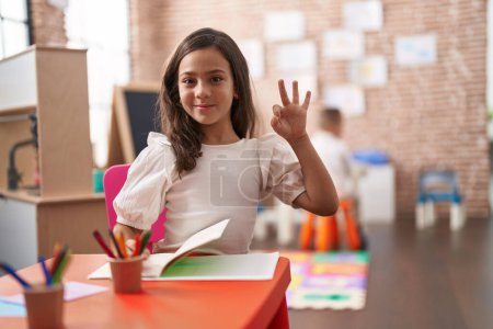 Photo for Little hispanic girl painting at the school doing ok sign with fingers, smiling friendly gesturing excellent symbol - Royalty Free Image