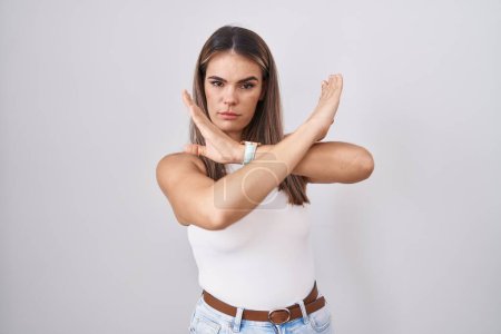 Foto de Mujer joven hispana de pie sobre fondo blanco expresión de rechazo cruzando brazos haciendo signo negativo, cara enojada - Imagen libre de derechos