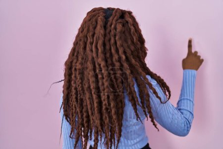 Photo for African woman standing over pink background posing backwards pointing ahead with finger hand - Royalty Free Image