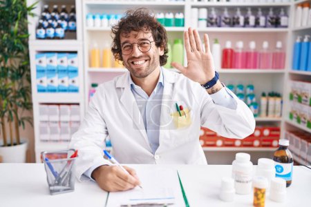 Foto de Joven hispano trabajando en farmacia renunciando a saludar feliz y sonriente gesto de bienvenida - Imagen libre de derechos