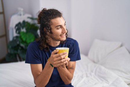 Foto de Joven hispano bebiendo una taza de café sentado en la cama en el dormitorio - Imagen libre de derechos