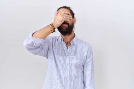 Téléchargez les photos : Homme hispanique avec barbe portant une chemise décontractée couvrant les yeux avec la main, l'air sérieux et triste. concept de non-visibilité, de dissimulation et de rejet - en image libre de droit