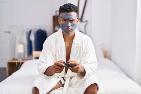 Téléchargez les photos : Young hispanic man wearing beauty face mask playing video games skeptic and nervous, frowning upset because of problem. negative person. - en image libre de droit
