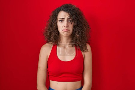 Photo for Hispanic woman with curly hair standing over red background depressed and worry for distress, crying angry and afraid. sad expression. - Royalty Free Image