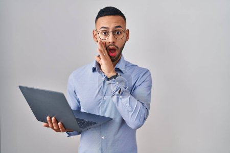 Photo for Young hispanic man working using computer laptop hand on mouth telling secret rumor, whispering malicious talk conversation - Royalty Free Image