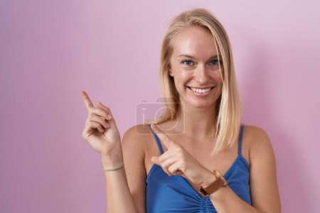 Téléchargez les photos : Jeune femme caucasienne debout sur fond rose souriant et regardant la caméra pointant avec deux mains et doigts sur le côté. - en image libre de droit