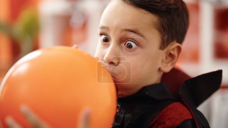 Photo for Adorable hispanic boy wearing halloween costume inflating balloon at home - Royalty Free Image