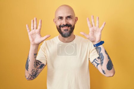 Photo for Hispanic man with tattoos standing over yellow background showing and pointing up with fingers number ten while smiling confident and happy. - Royalty Free Image