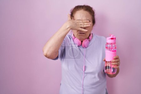 Photo for Senior woman wearing sportswear and headphones covering eyes with hand, looking serious and sad. sightless, hiding and rejection concept - Royalty Free Image