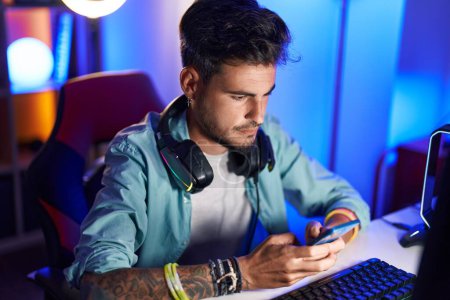 Téléchargez les photos : Jeune homme hispanique streamer en utilisant un ordinateur et un smartphone à la salle de jeux - en image libre de droit